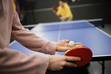 Cropped view of man holding racket and ball while playing table tennis in gaming club.
