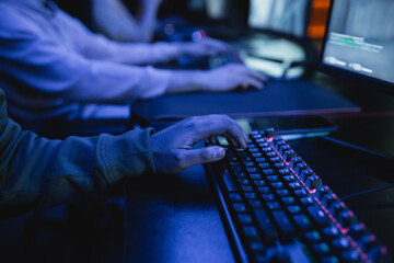 Cropped view of gamer using keyboard near computer monitor in gaming club with lighting.