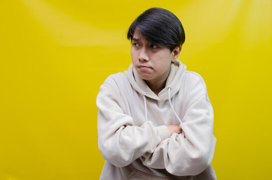 Thoughtful asian man in beige hoodie thinking and wondering with hand touching, rubbing head and face as thinking gesture isolated over yellow background