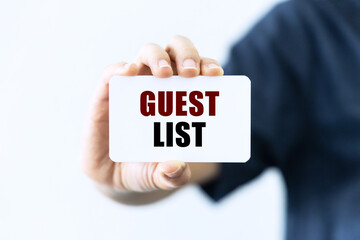 Guest list text on blank business card being held by a woman's hand with blurred background. Business concept about guest list.