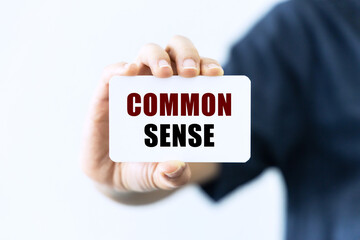 Common sense text on blank business card being held by a woman's hand with blurred background. Business concept about common sense.