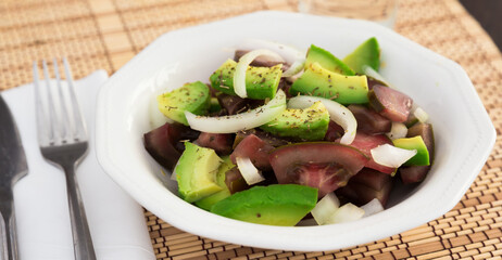salad of black tomatoes, avocado and onions in white ceramic bowl