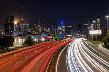 Cars travel on the Westgate Freeway at night in front of the Melbourne City Skyline