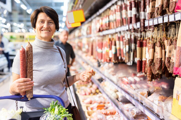 Elderly woman chooses sausage in supermarket