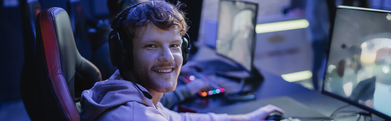 Cheerful young gamer in headphones looking at camera near computer in gaming club, banner. © LIGHTFIELD STUDIOS