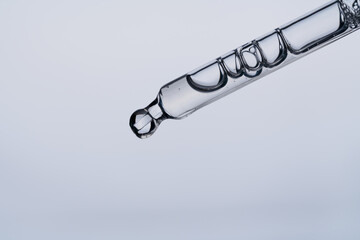 Facial serum in pipette on light blue background. Liquid gel or essential oil with bubbles macro. Anti aging cosmetic product with hyaluronic acid closeup. Innovation technology concept. Front view.