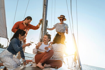 Group of happy friends drinking wine and relaxing on the sailboat during sailing in sea