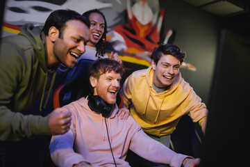 Cheerful multicultural friends playing computer game and rejoicing in gaming club.