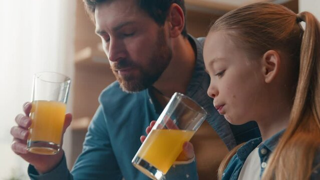 Happy family drinking orange juice at home Caucasian father with little daughter drink healthy fruit fresh at kitchen at breakfast dad with child kid girl talking enjoy organic juicy vitamin beverage