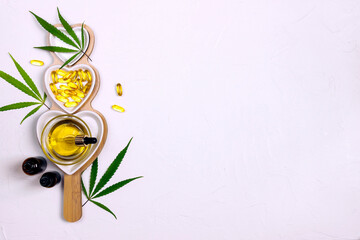 Heart dish with glass bottles, bowl with cbd oil, capsules and hemp leaves on white background. Top view, flat lay, copy space.