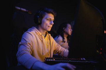 Young man in headphones playing computer game in cyber club with lighting.