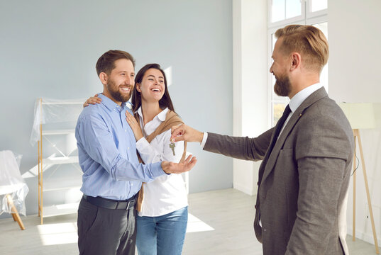 Happy young married couple accepts the key to a future new apartment. Smiling real estate agent congratulates happy customers on buying a house. Mortgage of real estate for sale.