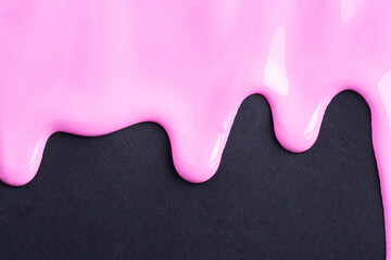 Pink liquid drops of paint color flow down on black paper. Abstract art. Pink paint dripping on the black wall