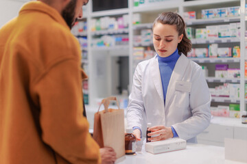 Young pharmacist selling medications to the customer.