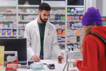Fototapeta premium Multiracial pharmacist selling medications to young woman.