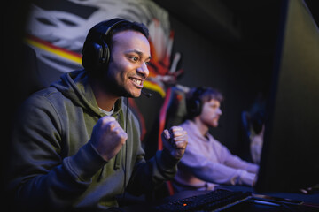 Excited indian gamer in headphones looking at computer monitor in gaming club. © LIGHTFIELD STUDIOS
