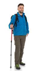 Full-length portrait of trekker with a backpack isolated on white background. Thirty years old man in blue jacket standing with trekking pole, posing in studio.