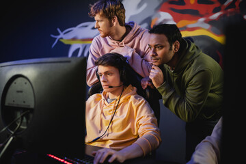 Fototapeta premium Focused indian man standing near friend playing video game on computer in gaming club.
