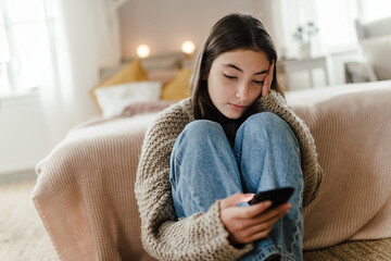 Teenage girl sitting on the floor and scrolling her smartphone.