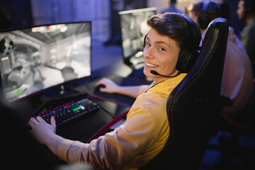 Naklejka premium Smiling man in headphones looking at camera while playing video game in cyber club.