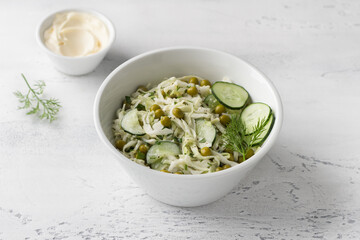 Salad with white cabbage, green peas, cucumber, herbs and mayonnaise sauce on a light blue background