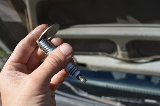 Hand Gapping a Spark Plug in Front of Car 