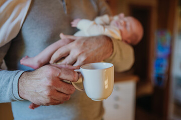 Close- up of father holding her newborn baby and cup of coffee.