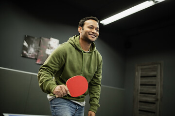 Cheerful indian man with racket playing table tennis in gaming club.