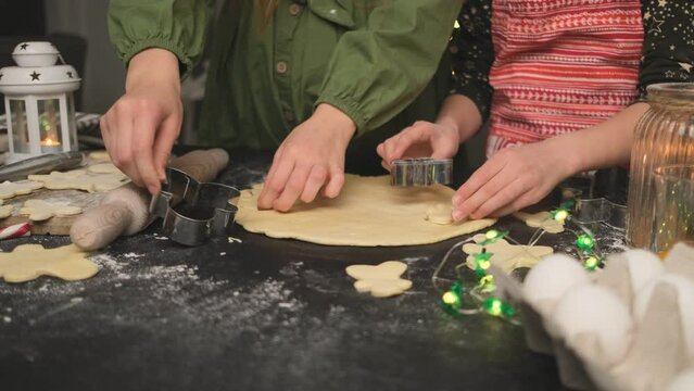 Girls cutting gingerbread men from dough using forms for cookies at home