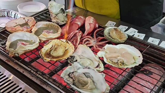 Chef using hand-held burner burning to burn hotate scallops and squid over a charcoal fire.