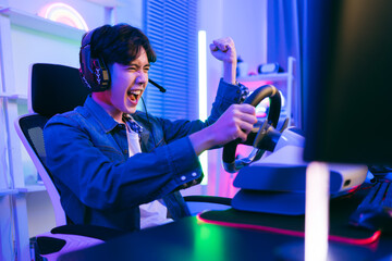 Asian male pro gamer playing an online car drive simulation game with steering wheel controller....