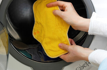 Female hands holding a yellow cloth pad inside a washing machine full of cloth bamboo washable sanitary napkins. Eco-friendly reusable fabric pads. Zero waste concept. Women hygiene concept