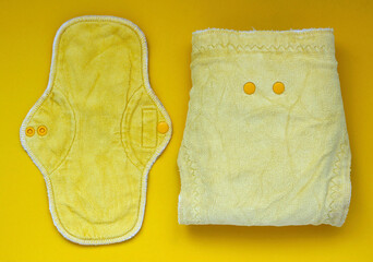 Yellow bamboo washable sanitary napkin and baby diaper on yellow background. Eco friendly reusable menstrual pad and baby diaper. Sustainable life concept, zero waste concept. Saving money concept.
