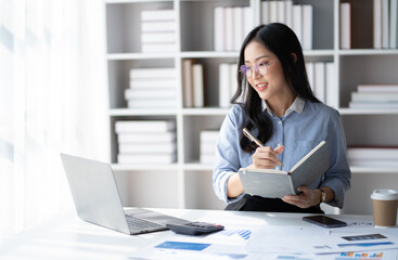 Young smart Asian businesswoman with glasses writing her idea while working in her office room.