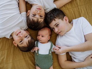 Three big brothers with their little newborn brother lying in bed. - obrazy, fototapety, plakaty
