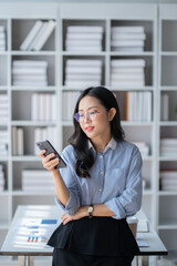 Happy Asian businesswoman using smartphone while working in hte office room.