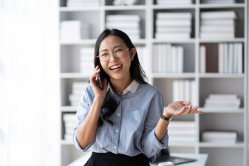 Beautiful Asian business woman having a phone call with her freind while sitting at the office desk.
