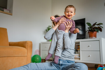 One young woman a mother playing at home on the floor with her child, holding one year old baby and...