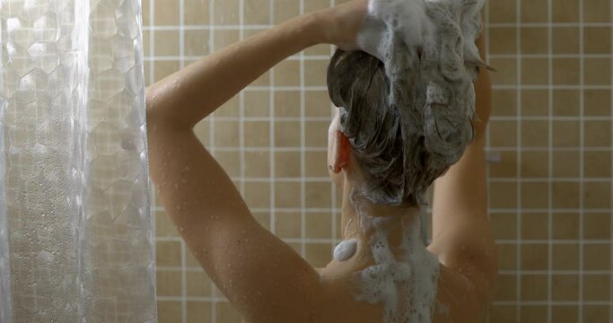 Young woman washing her hair in the shower with shampoo
