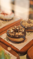 freshly baked or fried doughnuts covered in chocolate glazing with nuts crumble on top, on pastry or bakery display 