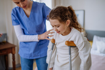 Young nurse helping to walk to little girl with broken leg.