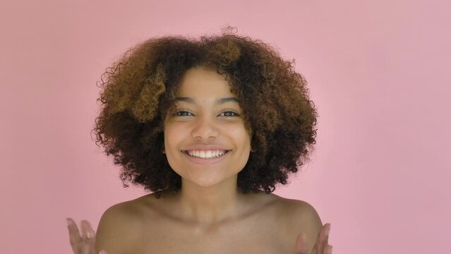 Emotions of joy, surprise, happiness. African girl jumping up with a joyful face and smile, portrait of a curly teenager beauty american on a pink background