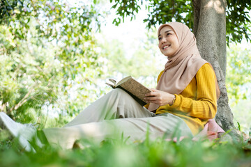 Education for Asian muslim women. Smiling beautiful student lady in hijab standing outdoors with workbooks in the park. Dreaming and learning concept.