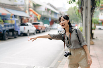 Fototapeta premium Smiling young Asian woman traveler hitchhiking on a road in the city. Life is a journey concept.