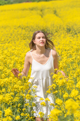 Fototapeta premium Beautiful woman with long blonde hair. He walks in the rapeseed field
