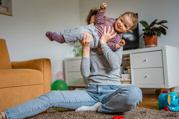 Obraz premium One young woman a mother playing at home on the floor with her child, holding one year old baby and tickling her, family playtime, early child development concept 