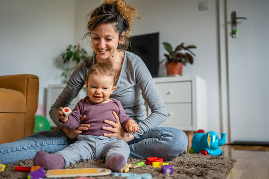 One young woman a mother playing at home on the floor with her one year old child, family playtime, early child development concept