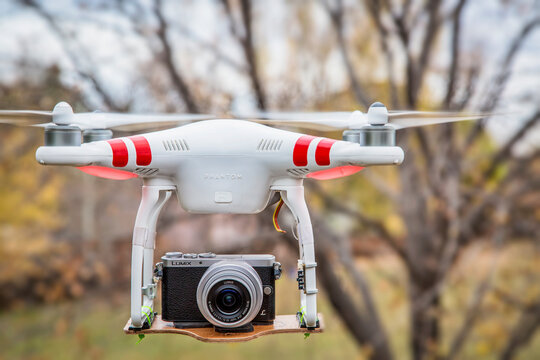 FORT COLLINS, CO, USA, November 2, 2014:  Airborne radio controlled Phantom 2 quadcopter drone flying with  the Panasonic Lumix GM1 camera mounted on a home made platform, blurred tree background.