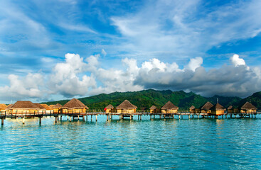 Overwater bungalows stretching out across the lagoon and a few catamarans in a quiet bay in Bora...