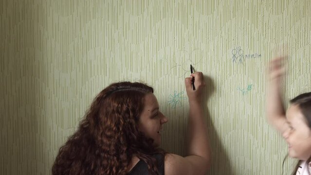 Curly red haired woman draw flower with marker on old wallpaper back view, little daughter swear emotionally waving fists. Space for painting, disorderly conduct, play pranks, paperhanging damage.